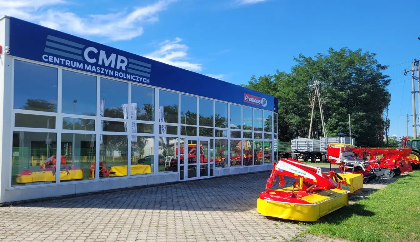 Przeszklona siedziba Centrum Maszyn Rolniczych z maszynami na trawniku.