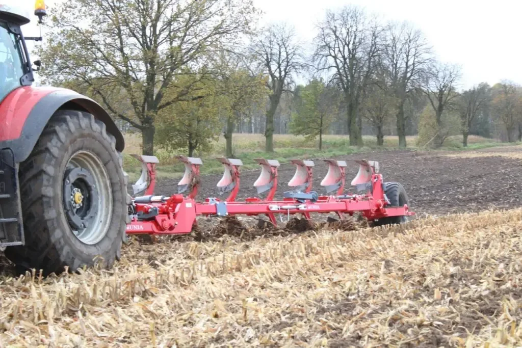 Unia Ibis XL Czerwony, wielokorpusowy pług obracalny Unia Ibis XL podpięty do ciągnika rolniczego podczas wykonywania orki na ściernisku.